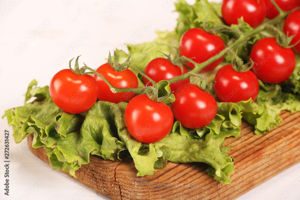 Ripe fresh Juicy organic brunch of cherry tomatoes on cutting board with Green Lettuce on a white table Ripe fresh Juicy organic brunch of cherry tomatoes on cutting board with Green Lettuce on a white table