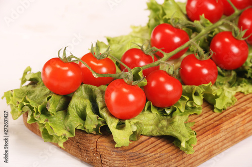 Ripe fresh Juicy organic brunch of cherry tomatoes on cutting board with Green Lettuce on a white table