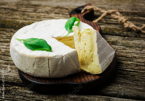 French cheese - round camembert with basil leaves on a wooden background 
