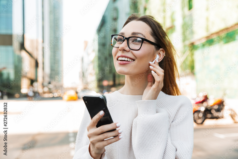 Photo closeup of happy smiling woman using cellphone and earpod while walking in big city street Photo closeup of happy smiling woman using cellphone and earpod while walking in big city street