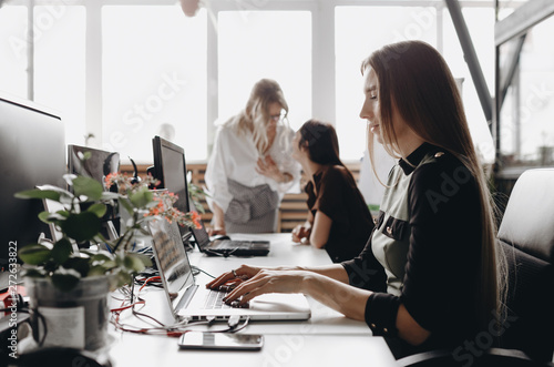 Young beautiful women dressed according to office dreskod are working  at the desks with a computer and laptops in a light modern open space office photo