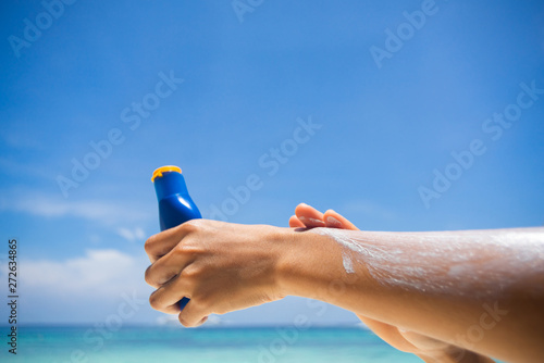Woman applying sunscreen on her hands from a bottle on the beach with the sea in the background. SPF sunblock protection concept.selective focus