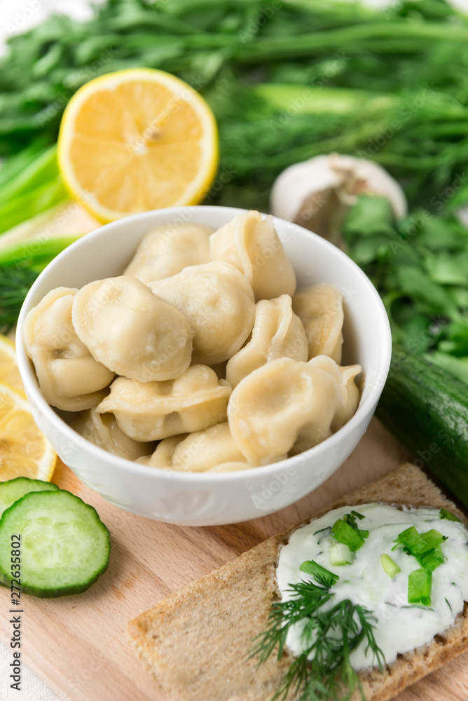 boiled meat dumplings in a plate, greens on a cutting Board, bread with yogurt and herbs boiled meat dumplings in a plate, greens on a cutting Board, bread with yogurt and herbs