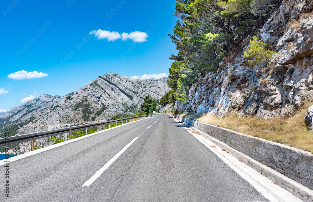 Naklejka premium Mountain highway with blue sky and rocky mountains on a background