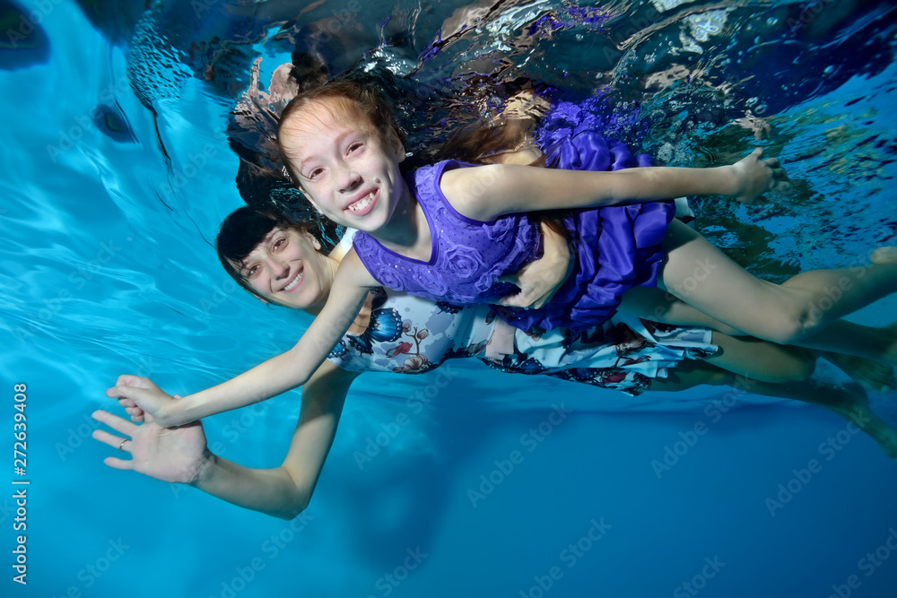 Happy family: mother and daughter hugging,floating underwater, holding hands. They smile and look at the camera. Underwater photography. Portrait. Horizontal orientation