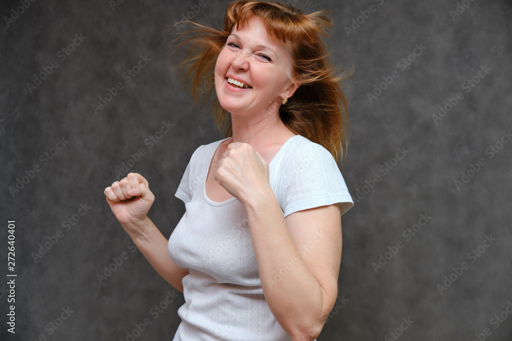 Studio portrait of a beautiful pretty woman age of 40 years on a gray background, smiling, showing different emotions, happy with life. In a white T-shirt with red hair. Directly opposite the camera. Studio portrait of a beautiful pretty woman age of 40 years on a gray background, smiling, showing different emotions, happy with life. In a white T-shirt with red hair. Directly opposite the camera.