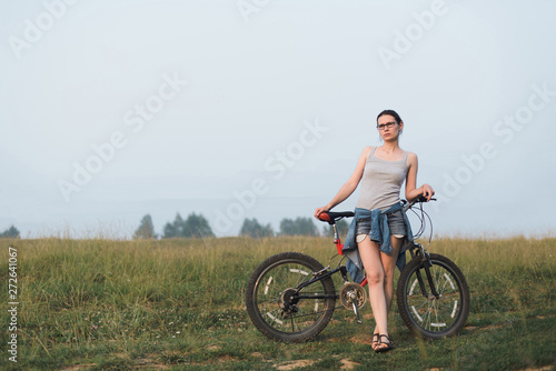 white caucasian young woman in casual clothing standing with bicycle in field, full body size view, lifestyles stock photo image