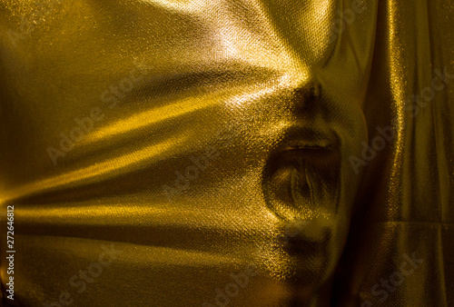 human face pressing through golden fabric