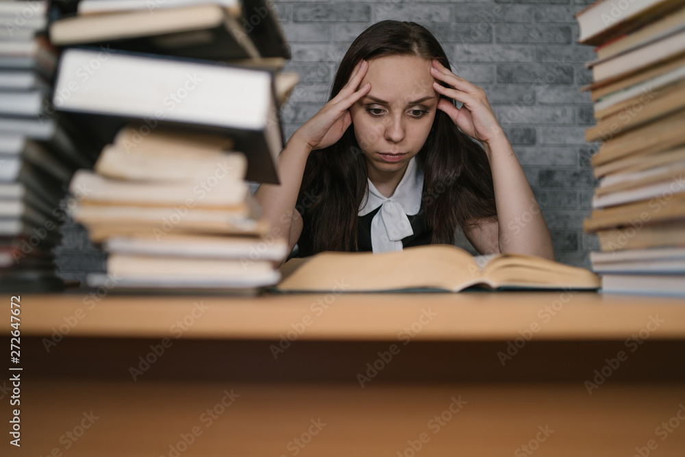 Woman student boring reading book at library with a lot of books in university. Student disheartened reading book for examination. Woman student boring reading book at library with a lot of books in university. Student disheartened reading book for examination.
