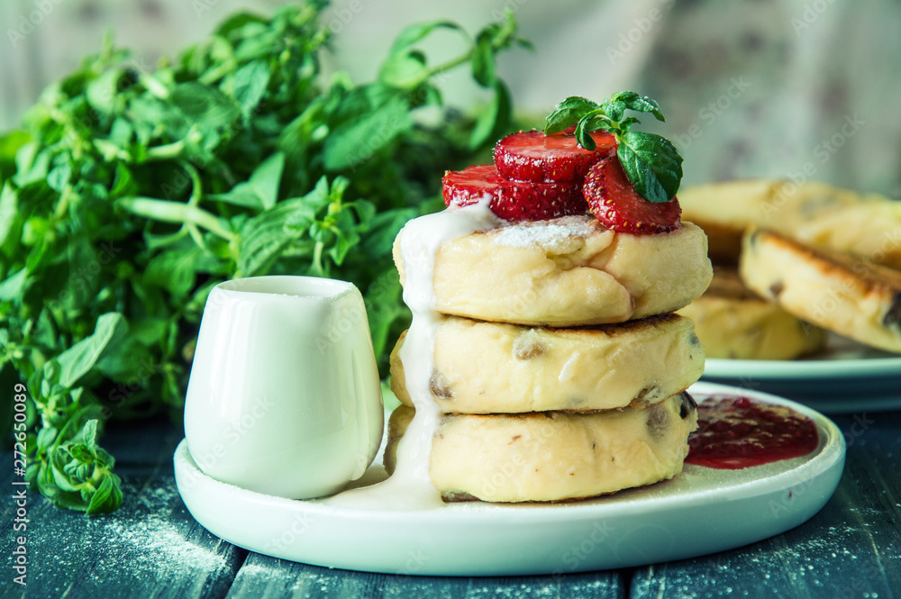 Close up, macro. Lush cheese pancakes, poured with cream and decorated with strawberries and mint. Close up, macro. Lush cheese pancakes, poured with cream and decorated with strawberries and mint.