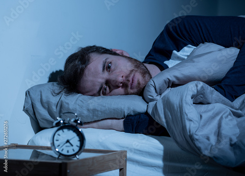 Young man in bed staring at alarm clock trying to sleep feeling stressed and sleepless