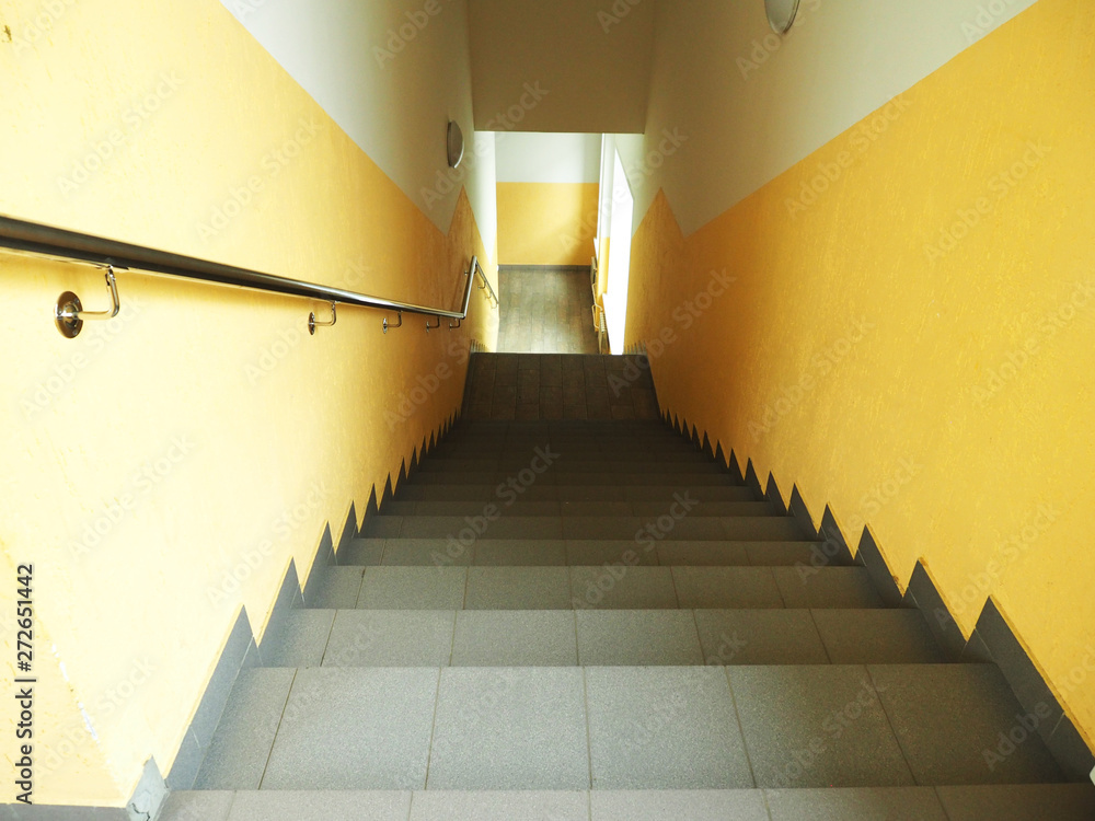 Obraz premium Steep and long stairs down, metal perilla, yellow walls, window below...