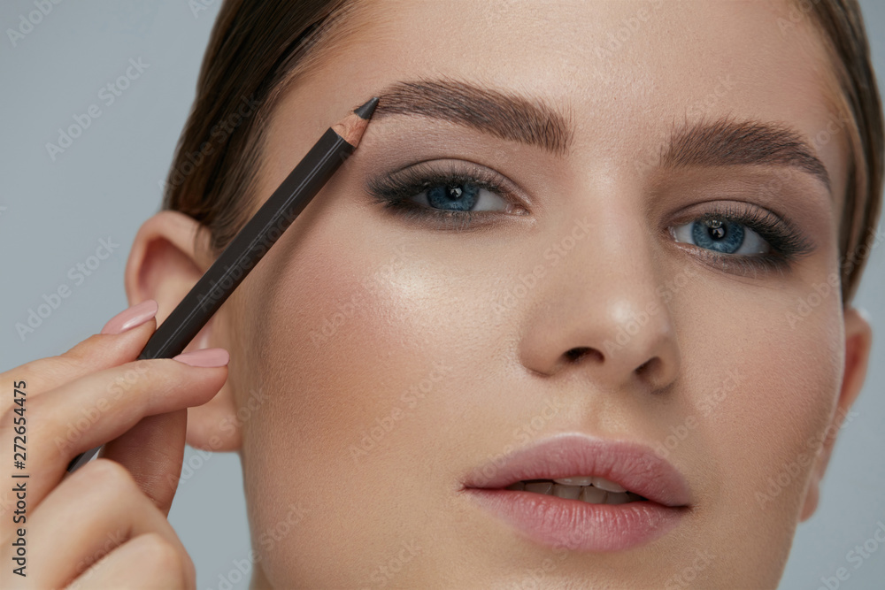Beauty makeup. Woman shaping eyebrow with brow pencil closeup