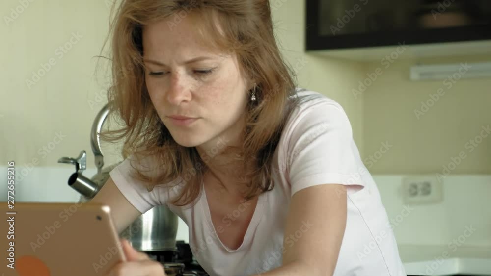 The woman in the kitchen uses the tablet, just woke up. Breakfast. Early morning The woman in the kitchen uses the tablet, just woke up. Breakfast. Early morning