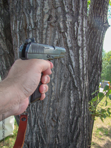 Pistol TT with leather strap. In your hand ready to shoot. The background is a tree. Summer, vertical layout.  photo