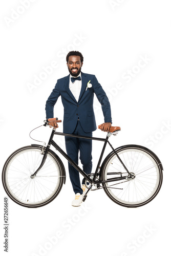 cheerful african american man in suit standing near bicycle isolated on white