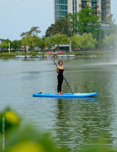 Young girl paddling on SUP board on a calm lake at city. Sup surfing woman. Awesome active training in outdoor.