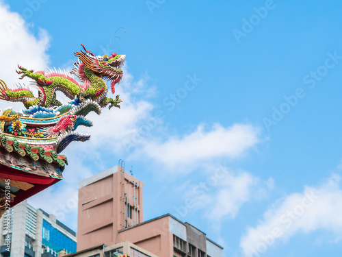 Looking up dragon sculpture on top of chinese temple roof against the blue sky and clouds with copy space. Temple in the city.