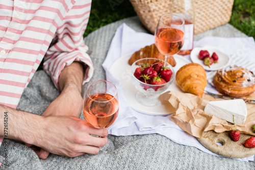 Man's hand holding glass of rose wine, summer picnic with cheese and wine