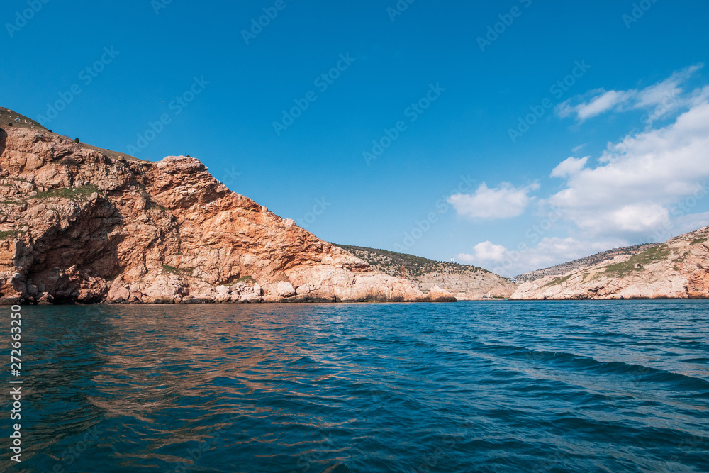 Orange island mountain coastline, blue sky with clouds and ocean water, summer travel landscape