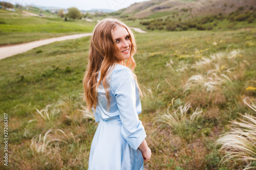 Young long-haired girl in a blue dress on a beautiful summer field.