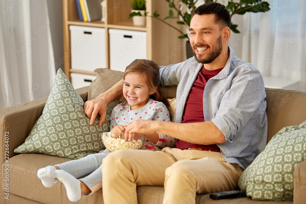 family, fatherhood and people concept - happy father and daughter with popcorn watching tv at home family, fatherhood and people concept - happy father and daughter with popcorn watching tv at home
