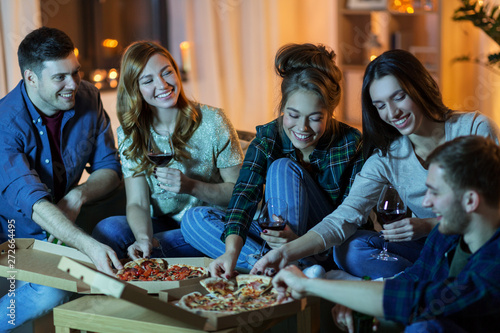 friendship  food and leisure concept - happy friends eating pizza and drinking non-alcoholic wine at home in evening