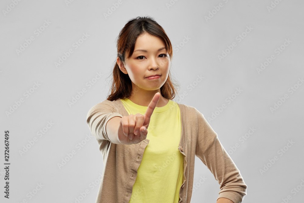 people, prohibition and rejection concept - young asian woman threatening with finger over grey background people, prohibition and rejection concept - young asian woman threatening with finger over grey background