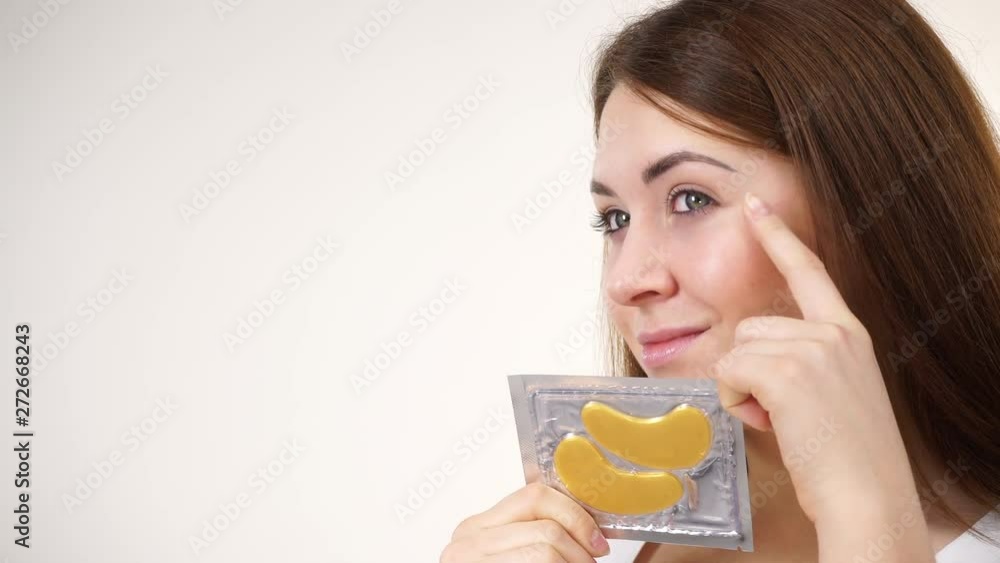 Young woman ready to applying golden collagen patches under eyes, against white. Mask removing wrinkles and dark circles. Girl taking care of delicate skin around eyes. Beauty treatment. Skincare Young woman ready to applying golden collagen patches under eyes, against white. Mask removing wrinkles and dark circles. Girl taking care of delicate skin around eyes. Beauty treatment. Skincare