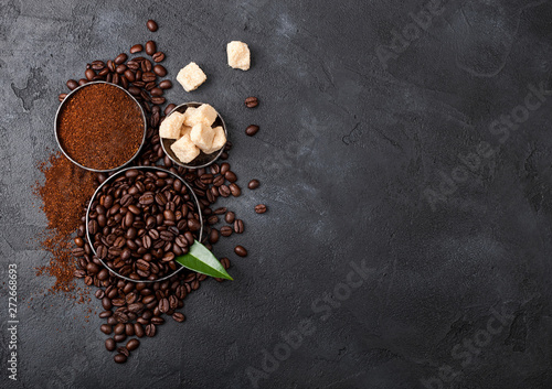 Fresh raw organic coffee beans with ground powder and cane sugar cubes with coffee trea leaf on black background.