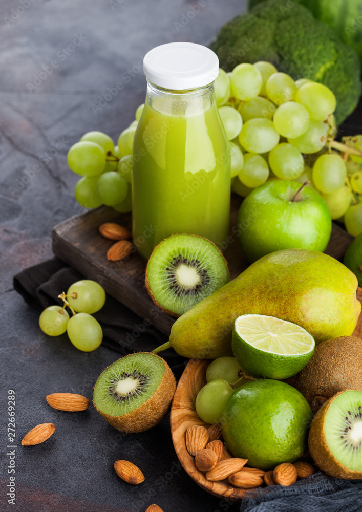 Glass bottle of fresh smoothie juice organic green toned fruit and vegetables on stone kitchen background. With almond nuts in bowl. Glass bottle of fresh smoothie juice organic green toned fruit and vegetables on stone kitchen background. With almond nuts in bowl.
