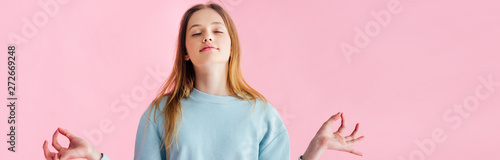 panoramic shot of pretty teenage girl with closed eyes meditating isolated on pink