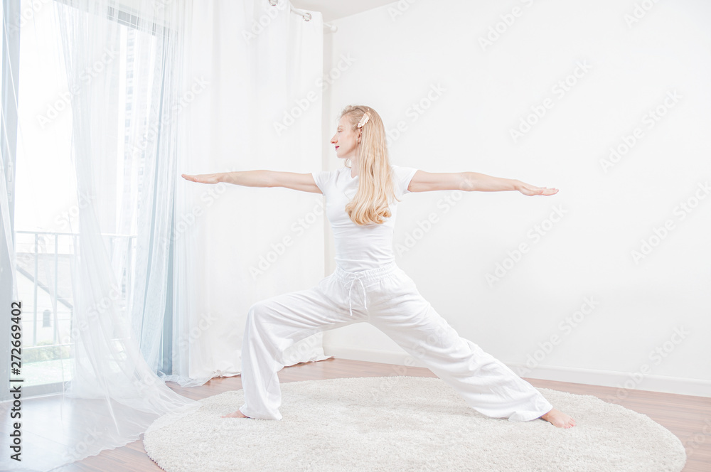Beautiful woman is practicing yoga at home, girl doing Virabhadrasana exercise, standing in Warrior pose Beautiful woman is practicing yoga at home, girl doing Virabhadrasana exercise, standing in Warrior pose