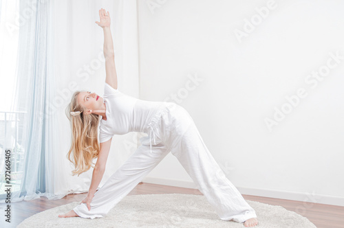 Beautiful woman is practicing yoga at home, girl doing Utthita Trikonasana exercise, extended triangle pose