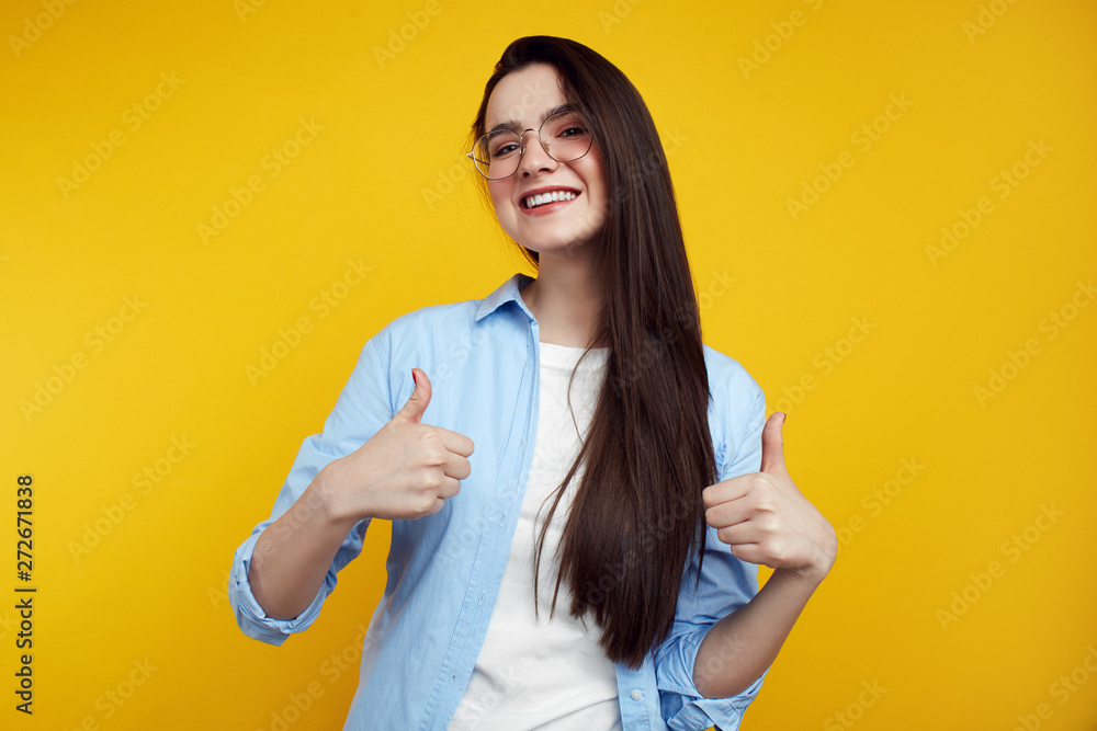 Cheerful attractive female with eyeglasses showing thumbs up isolated on the yellow background Cheerful attractive female with eyeglasses showing thumbs up isolated on the yellow background