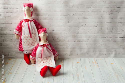 Two tilde dolls in red dresses, and white aprons, and in red kalpaks sit on a light background. Interior dolls. There is a place for text. The concept of needlework, and handmade. photo