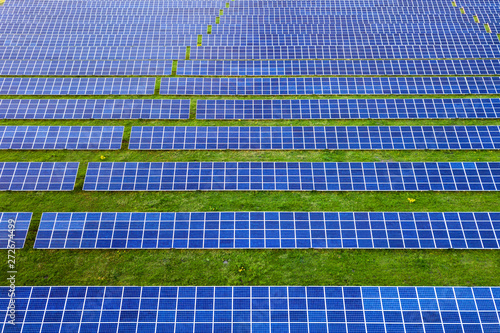 Large field of solar photo voltaic panels system producing renewable clean energy on green grass background.