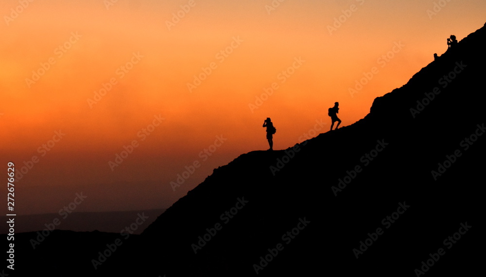Silhouette of people walking on a mountain in front of a sunrise