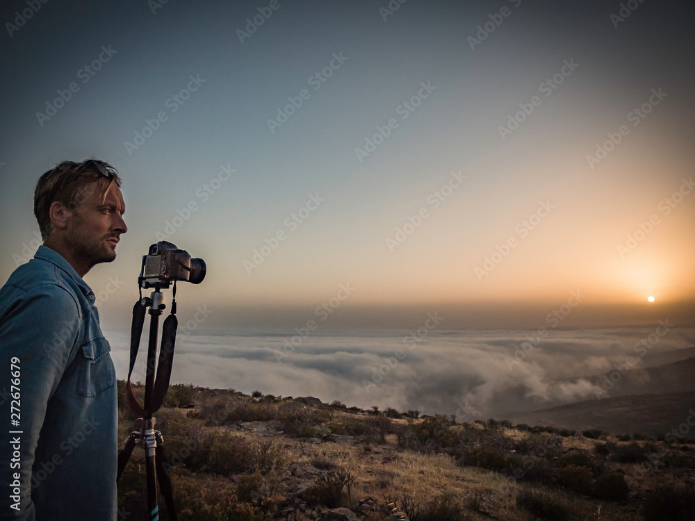 Man taking photograph of a beautiful sunset above the clouds on top of a mountain