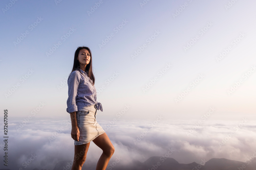 Portrait of a woman on top of a mountain above the clouds during sunset