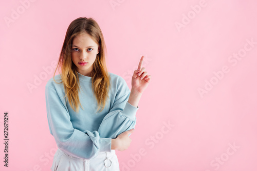 sad teenage girl pointing with finger isolated on pink photo