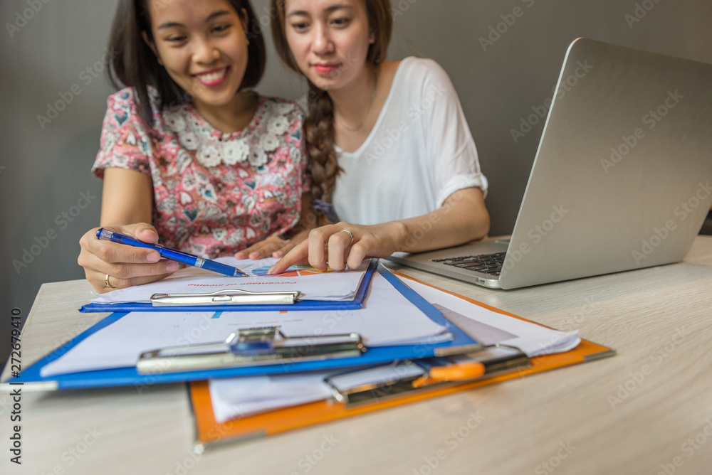 Two happy young girl reading document next to laptop Two happy young girl reading document next to laptop