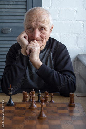 An old man is sitting in front of a chessboard, thinking about the next move in a chess game photo