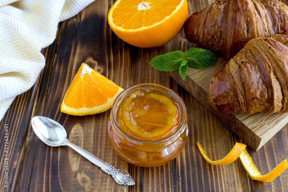 Homemade orange marmalade in the glass jar and croissants on the brown wooden background Homemade orange marmalade in the glass jar and croissants on the brown wooden background
