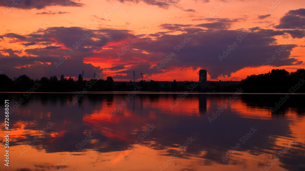 Amazing orange sunset over the horizon with a silhouette of isolated tower. Darkness and dramatic sky in beautiful landscape. Reflection and symmetry of the clouds. Amazing orange sunset over the horizon with a silhouette of isolated tower. Darkness and dramatic sky in beautiful landscape. Reflection and symmetry of the clouds.
