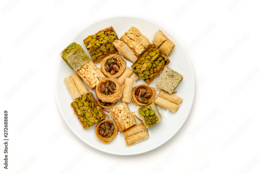 Traditional oriental sweets in white plate with different nuts on a white table, top view