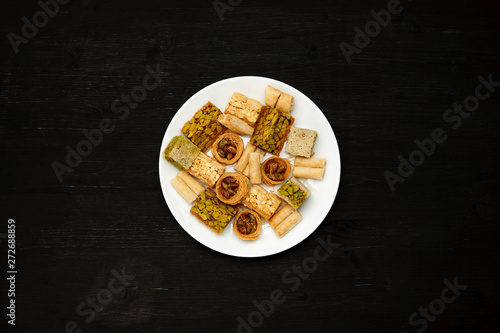 Traditional oriental sweets in white plate with different nuts on a black table, top view