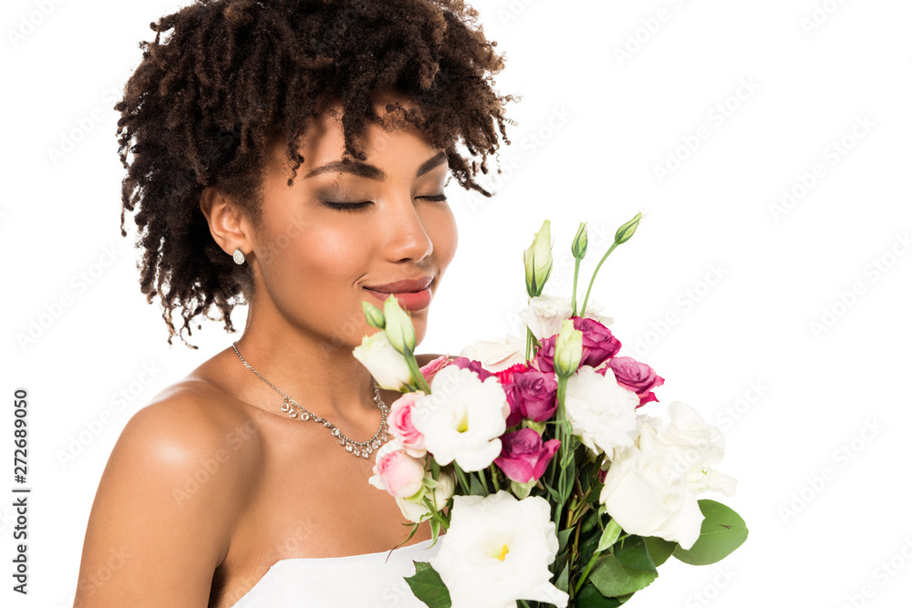 cheerful african american bride holding bouquet while smelling flowers isolated on white