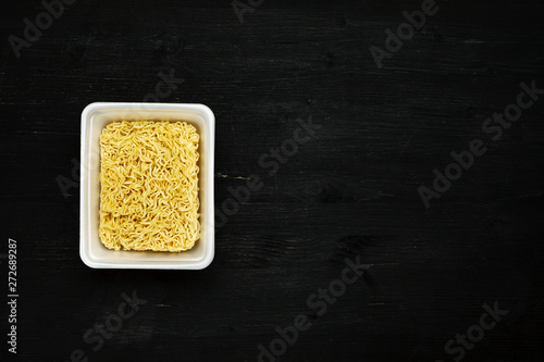 Instant noodles in container on a black wooden table, top view, text space