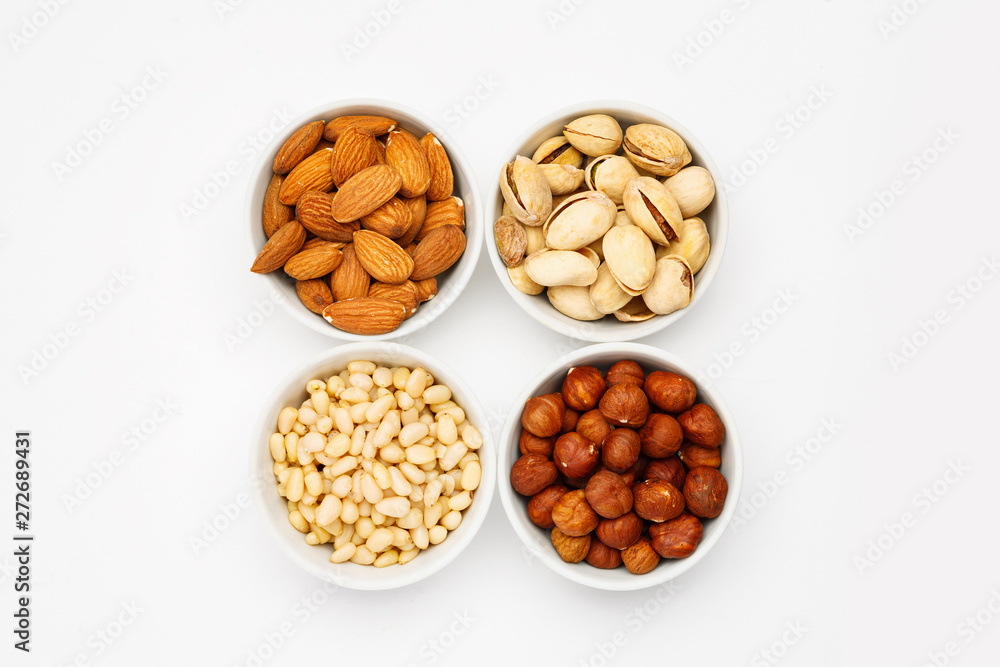 Different nuts in ceramic bowls on a white table, top viev Different nuts in ceramic bowls on a white table, top viev